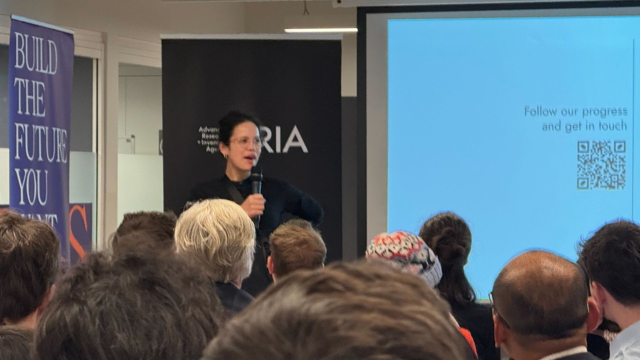 Woman holding a microphone speaking to an audience.